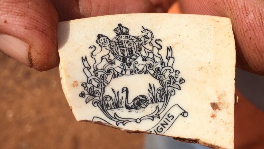 A small fragment of crockery with the WA insignia held between a man's thumb and finger