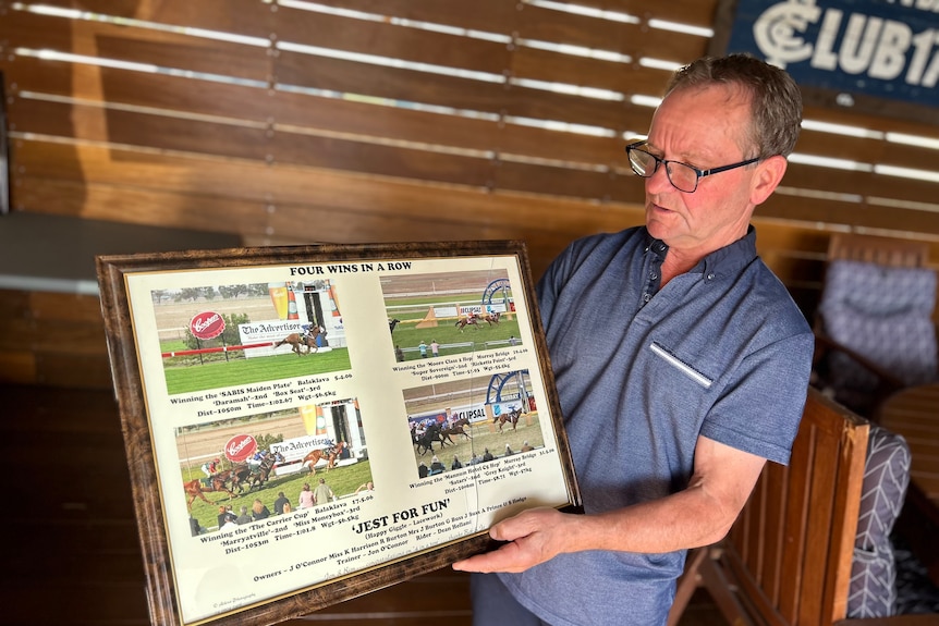 A man holding framed memorabilia of horse racing