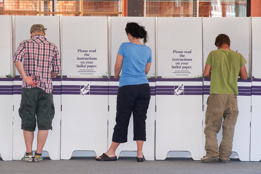 Three people stand at a row of polling booths in Alice Springs.