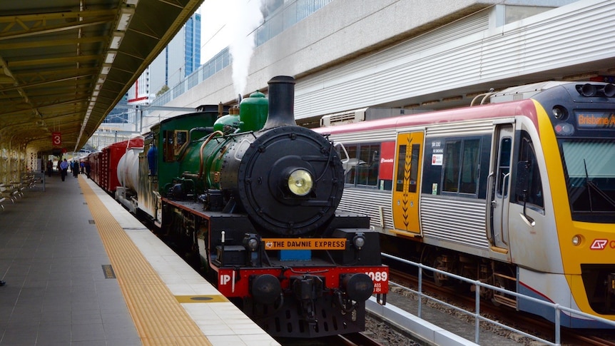A green steam train, next to a modern train in Brisbane.