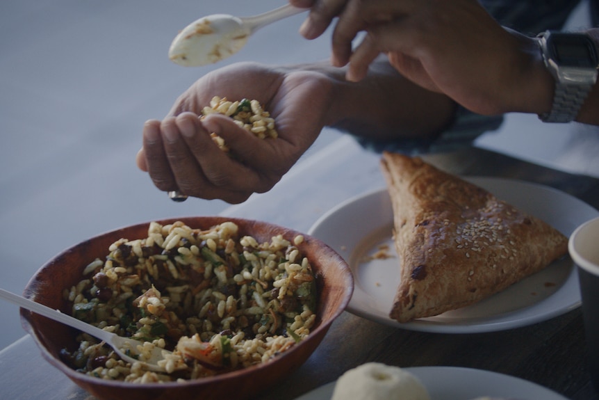 A person spooning some mixed rice into their hand.