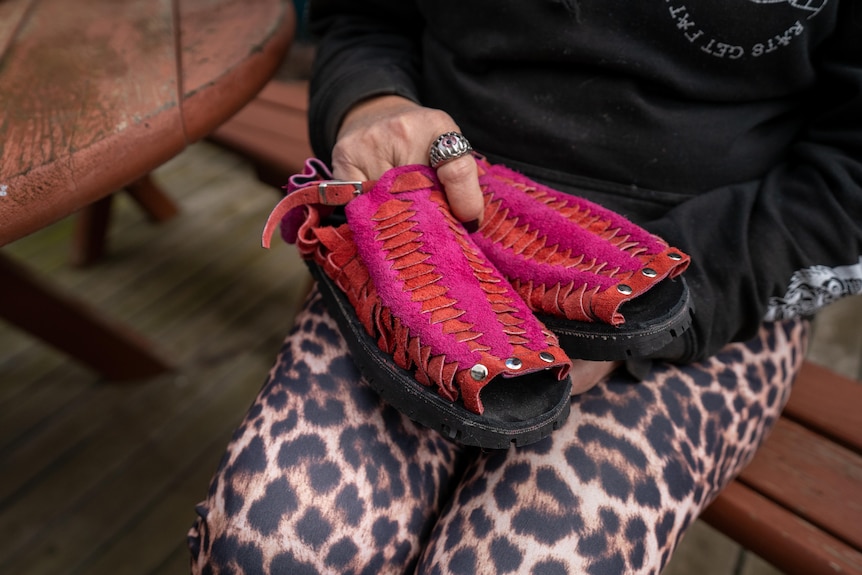 a pair of brightly coloured shes, with a tyre sole, held on the lap of the cobbler.