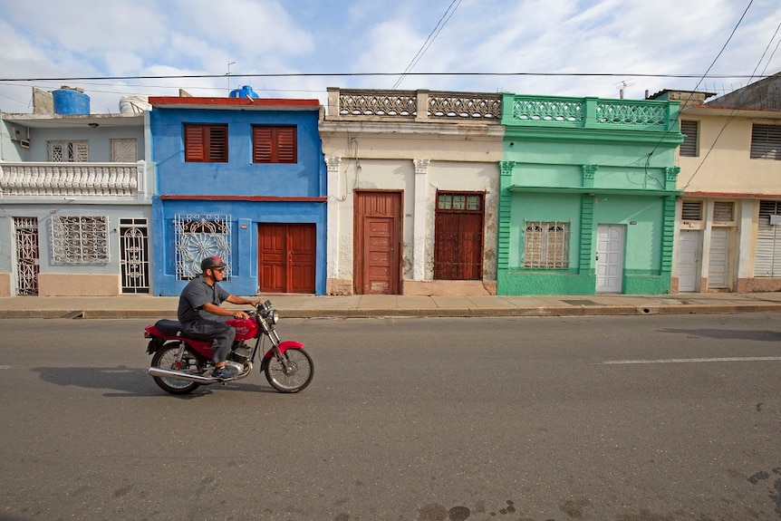 Un homme conduit sa moto dans une rue colorée de Cienfuegos, Cuba.