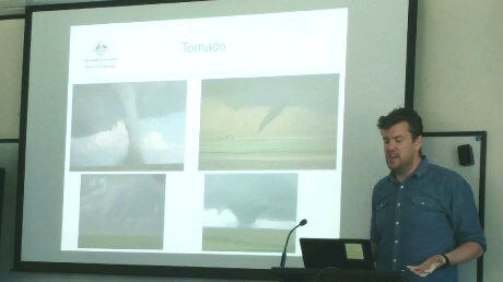 Man stands at podium in front of screen with information about tornados