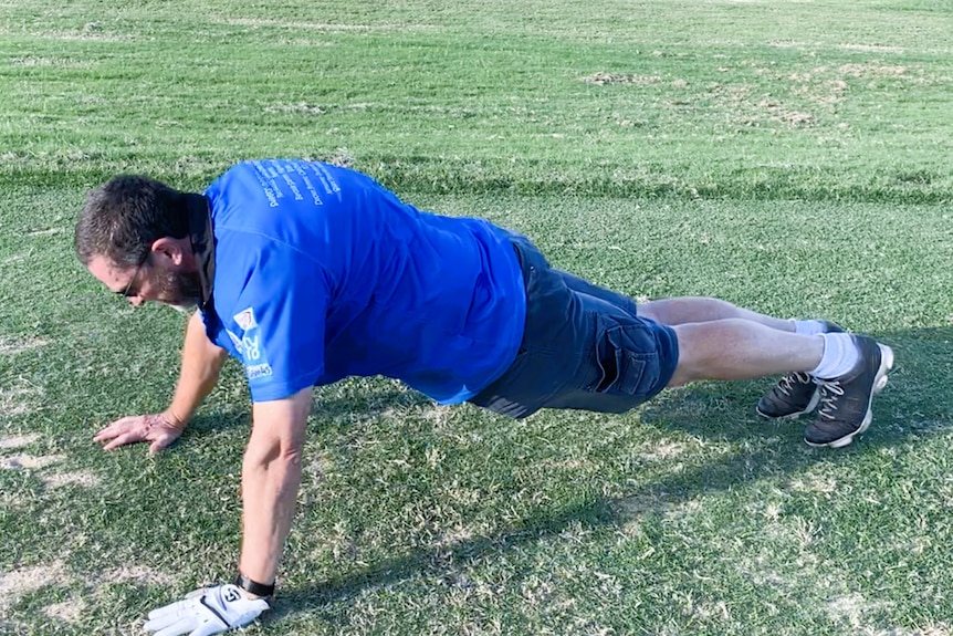 A man in a blue polo shirt doing a push up on a golf course.