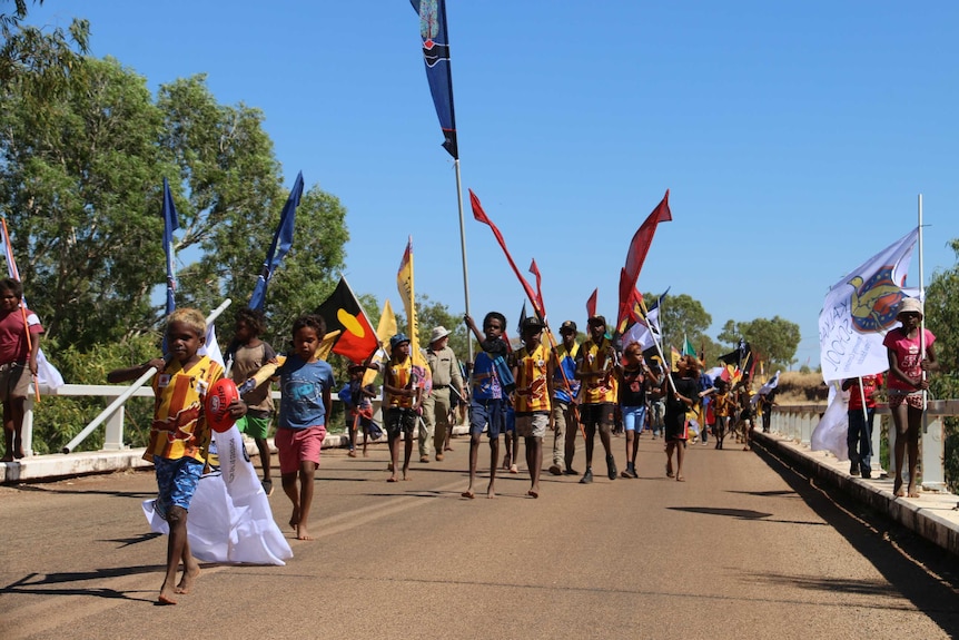 Children with flags walk across a bridge