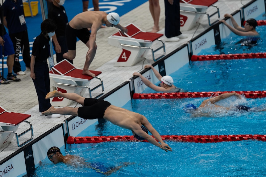 Swimmers jumping into an indoor pool 