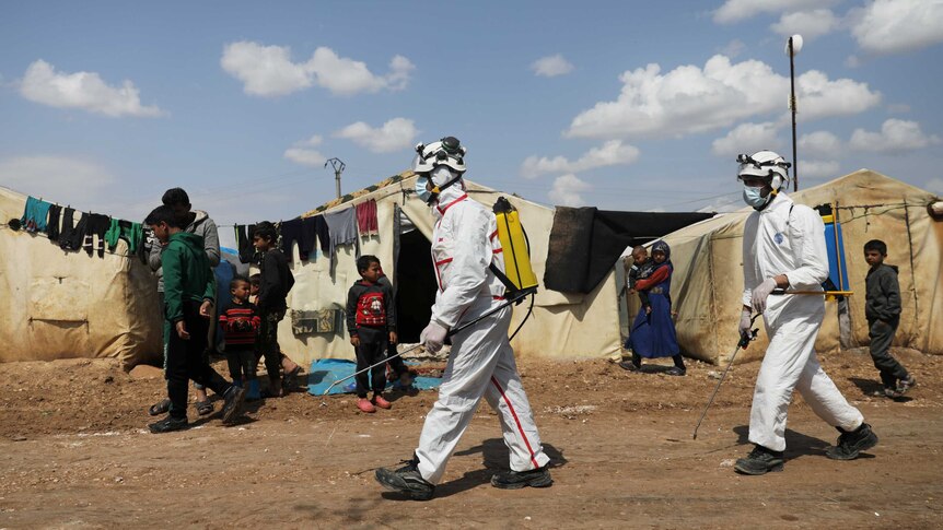 Men in hazmat gear spray disinfectant at a refugee camp