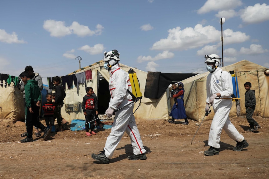 Men in hazmat gear spray disinfectant at a refugee camp