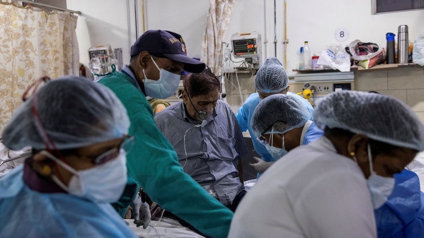 A man wearing an oxygen mask is surrounded by doctors and nurses in an Indian hospital.