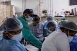 A man wearing an oxygen mask is surrounded by doctors and nurses in an Indian hospital.