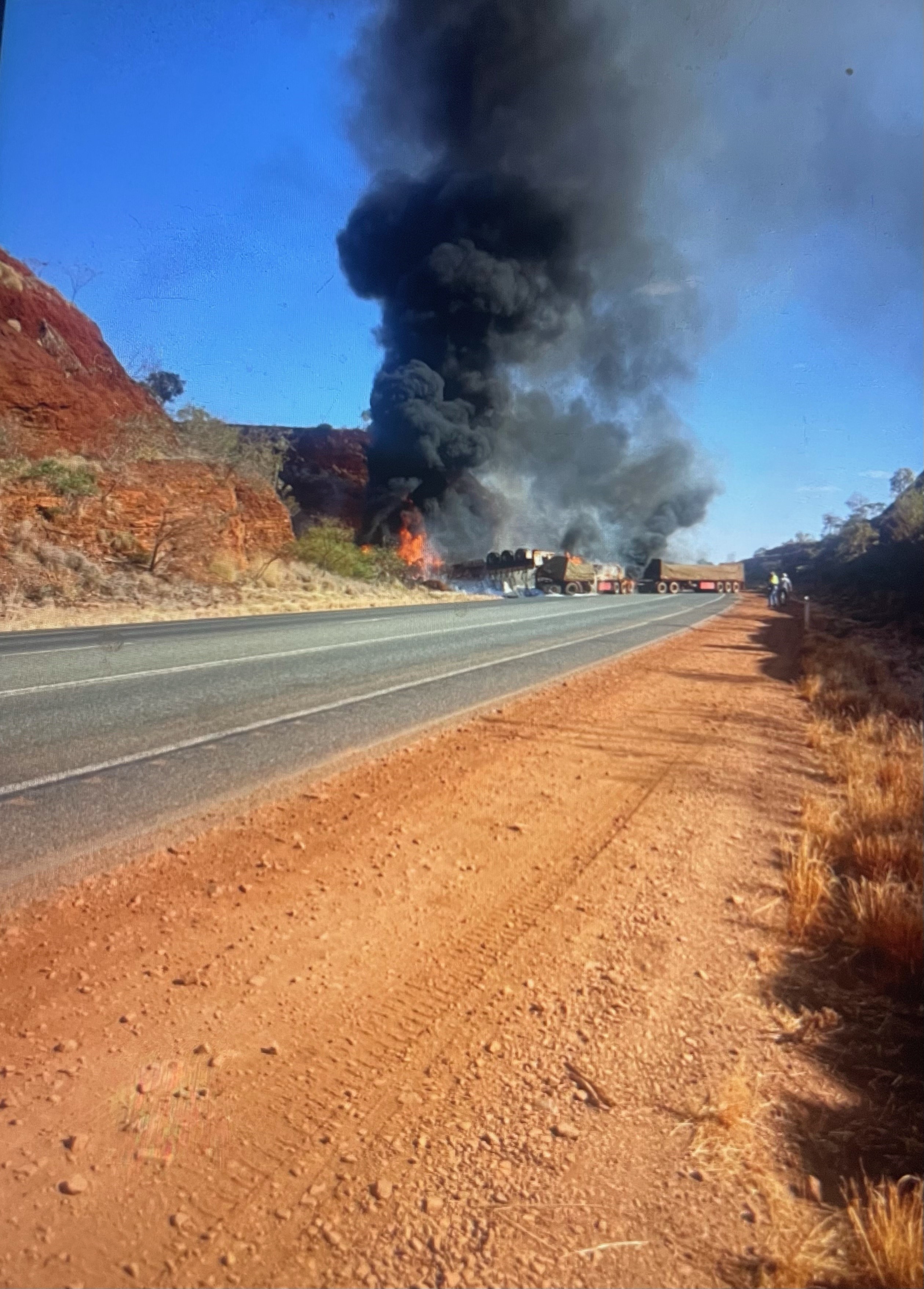 A large plume of smoke comes from a fire on a regional road next to a rocky hill