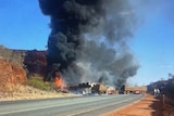 Thick, dark smoke rises above a crash scene on a desert highway pictured from several hundred metres away.