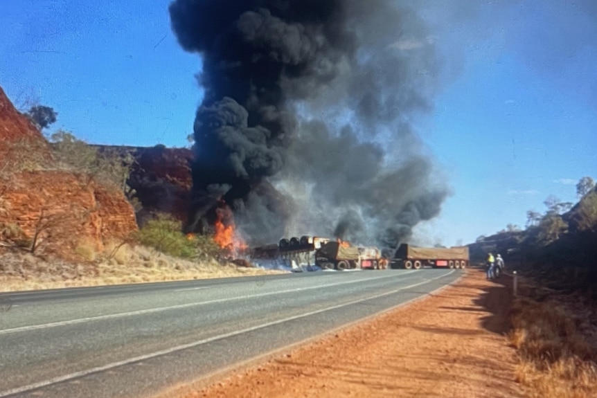 A large plume of smoke comes from a fire on a regional road next to a rocky hill