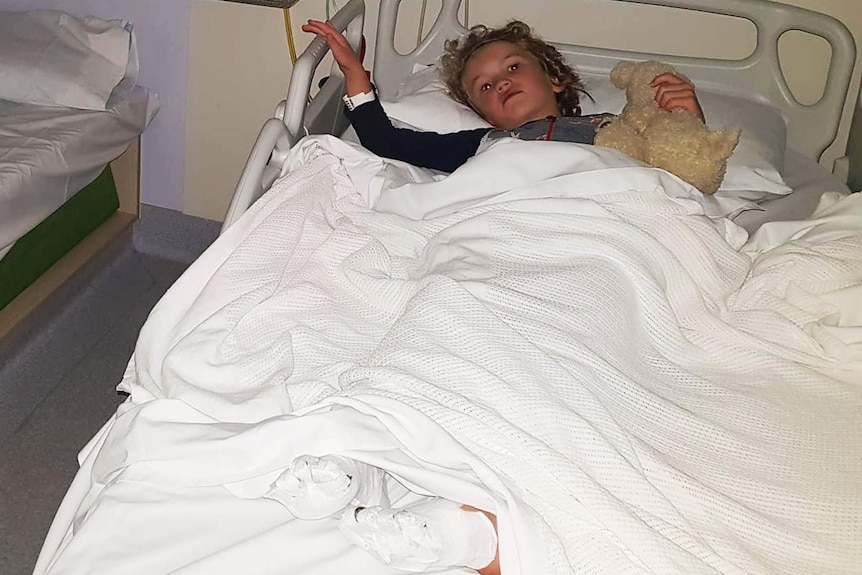 Kai Dight in his hospital bed with bandages around his feet.