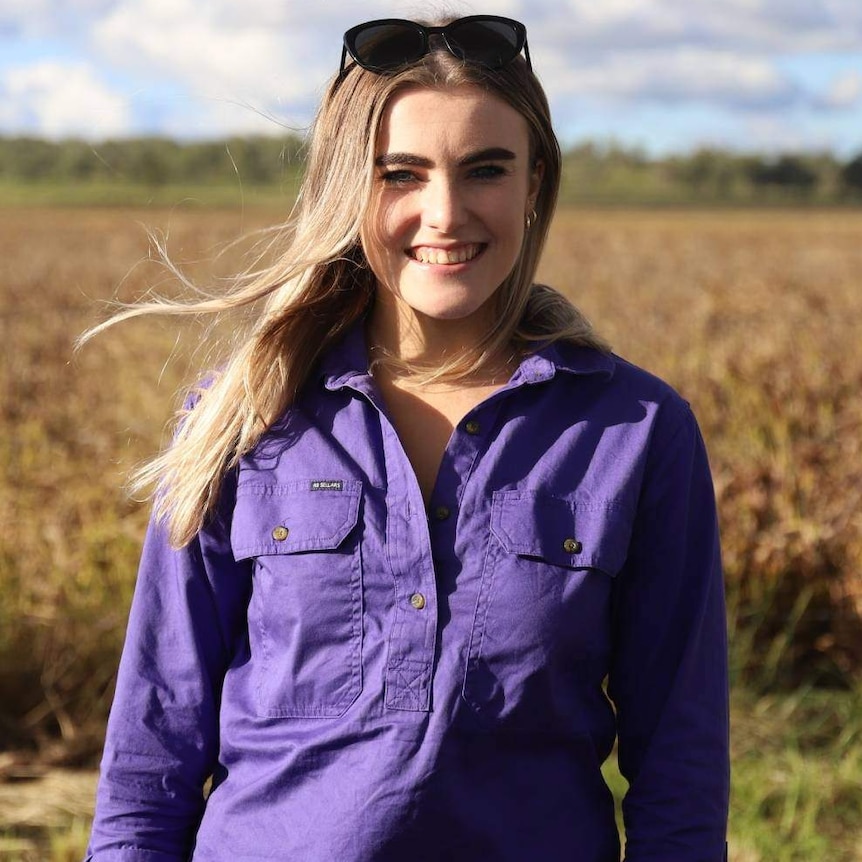 A woman wearing a purple shirt stands in a field.