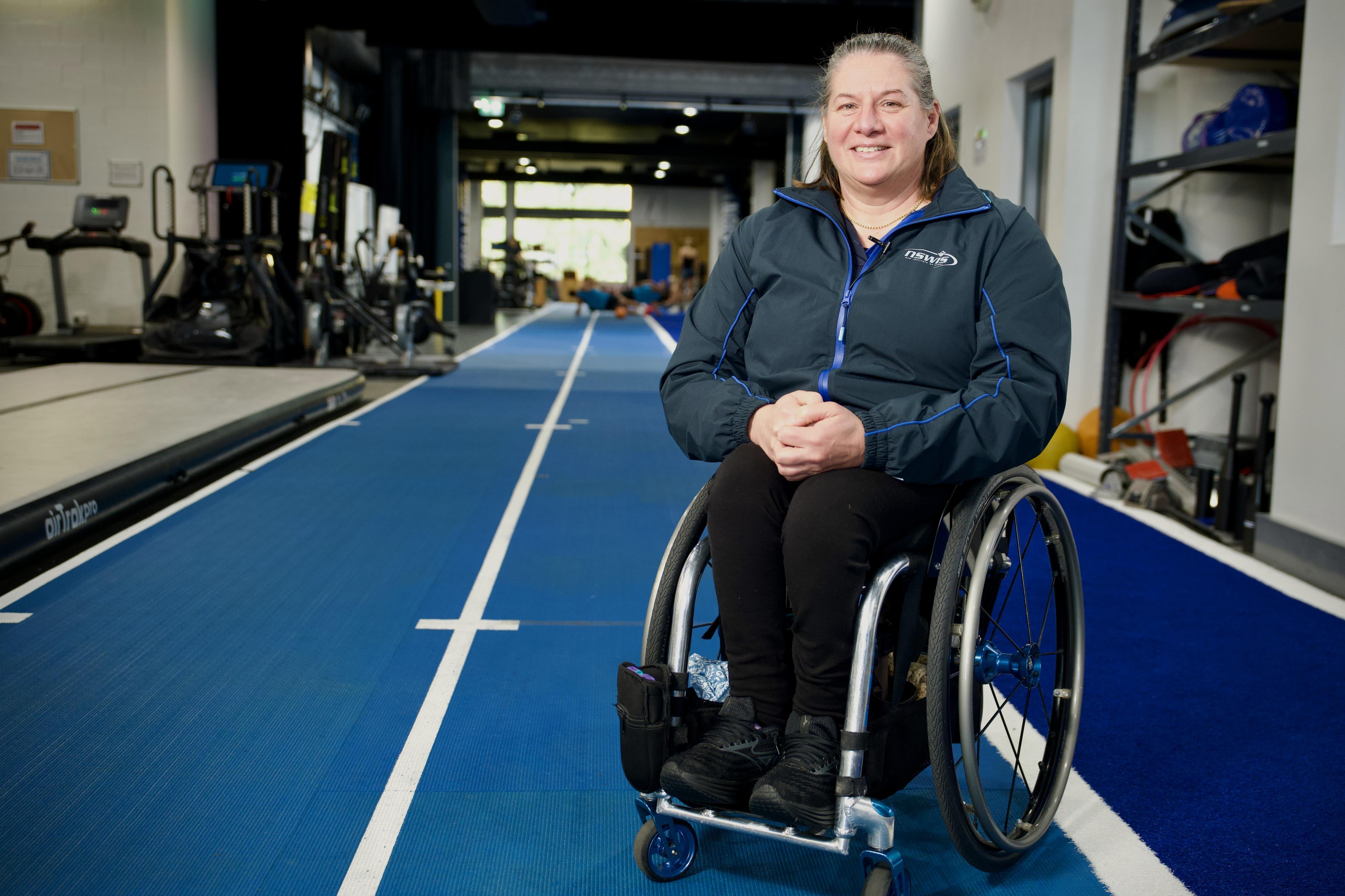Paralympic legend and coach Louise Sauvage sits in her wheelchair on an indoor track and smiles