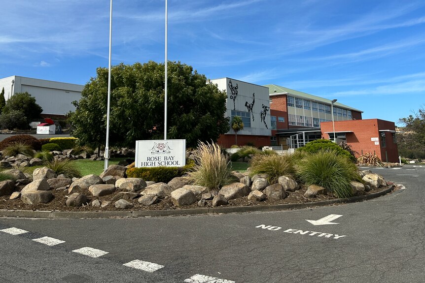 The entrance Rose Bay High School where a sign is mounted on one of two flagpoles at the end of a driveway.