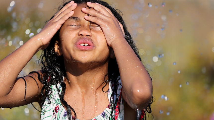 A young girl pushes her hair back while running through a sprinkler 