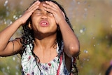 A young girl pushes her hair back while running through a sprinkler 