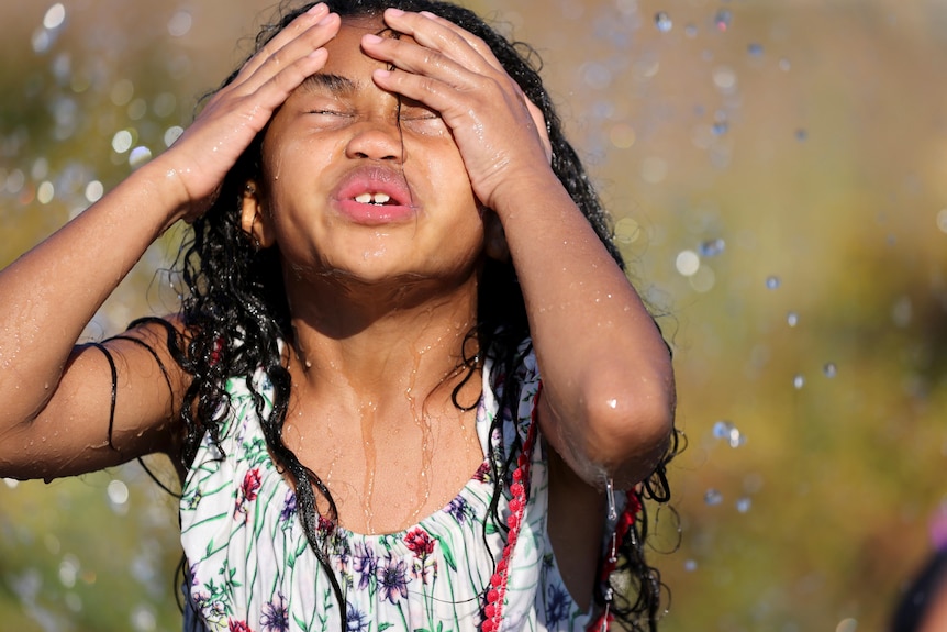 A young girl pushes her hair back while running through a sprinkler 