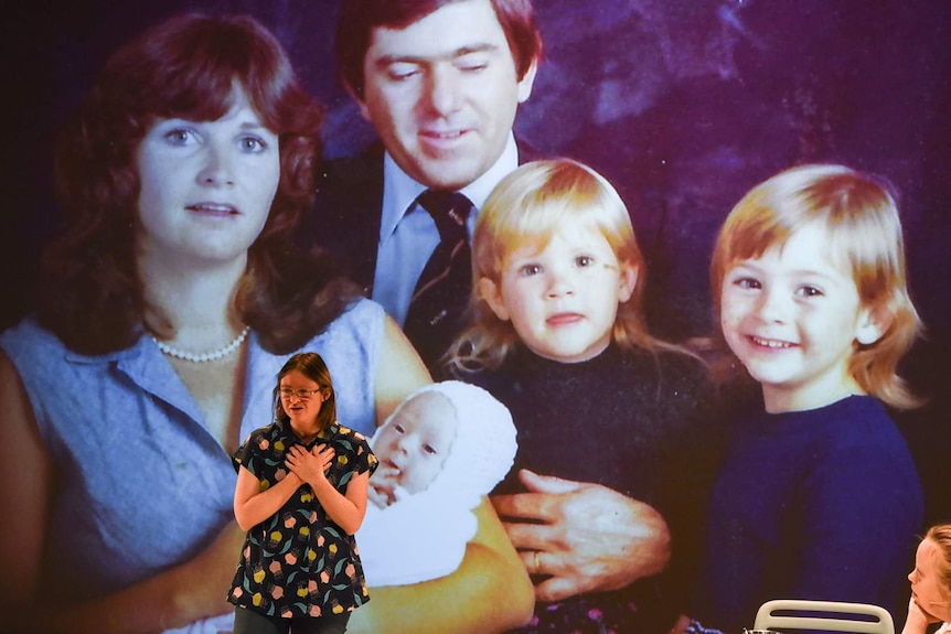 Woman on stage with large photograph of family projected onto back wall of stage behind her.