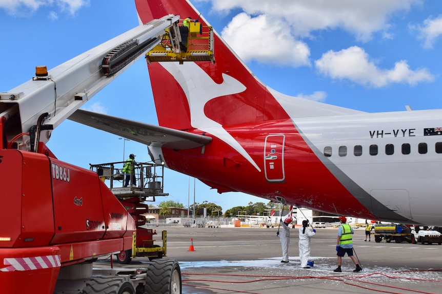 A Qantas plane on the tarmac, with workers around it.