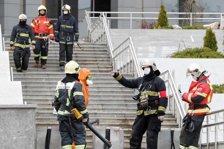 Firefighters in full gear and masks stand on the concrete steps of a hospital
