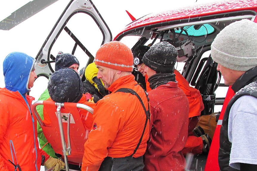 Australian Antarctic Division staff help load an ill expeditioner into a helicopter in Antarctica.