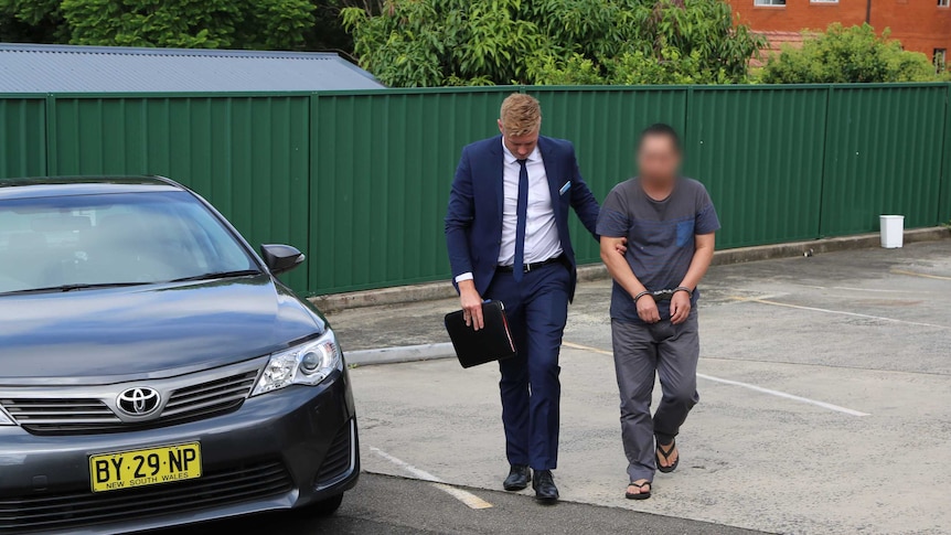 A 56-year-old man is lead away by a detective in a car park after being arrested in Cherrybrook.