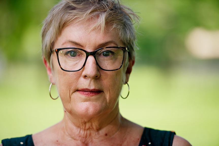 A middle-aged woman with short hair and glasses looks at the camera
