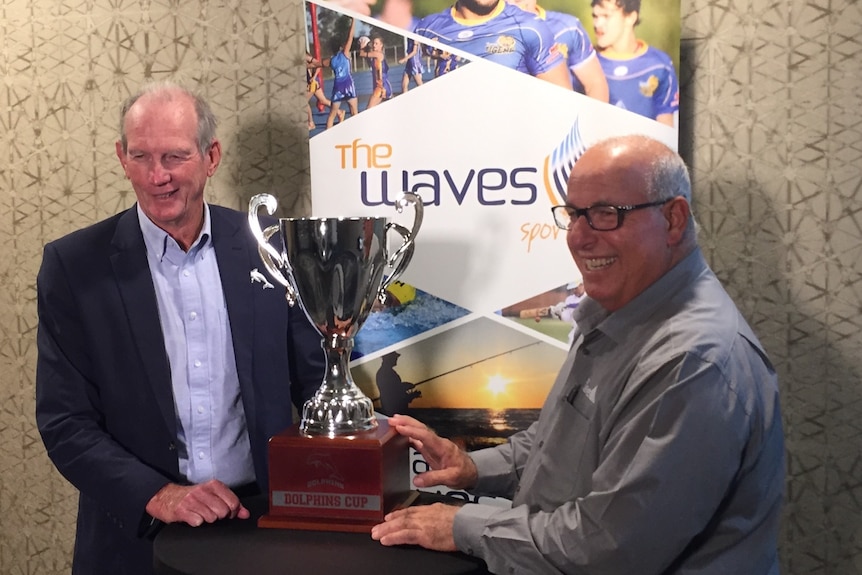 Two older men pose for a photo with new dolphins cup trophy