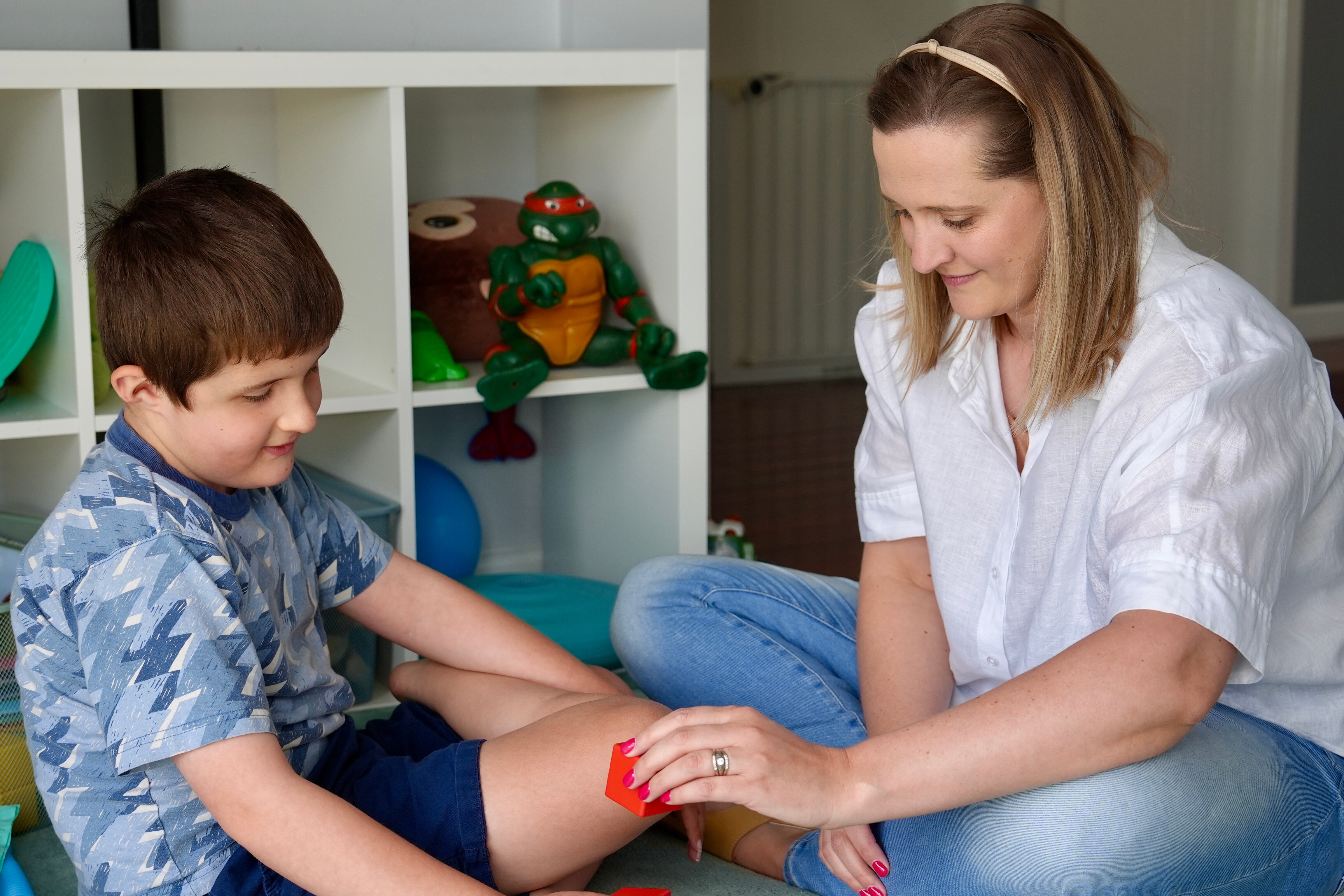 Uma mulher brinca com o filho sentado no chão.