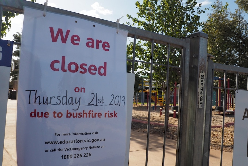 A sign secured to a metal school gate with zip ties reads 'We are closed on Thursday due to bushfire risk'.