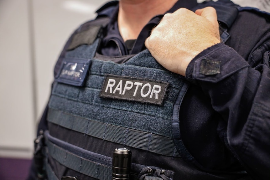 A close up of a man wearing a navy blue NSW Police vest with a patch that says "Raptor".