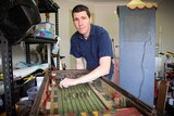 Repairer Jason Coultis stands over his arcade horse racing gambling game he restored.