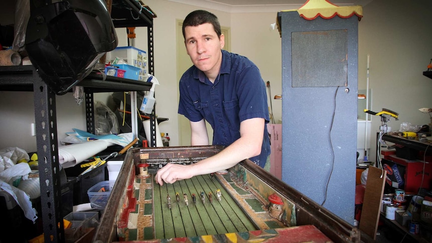 Repairer Jason Coultis stands over his arcade horse racing gambling game he restored.