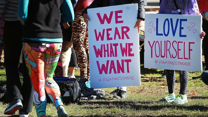 People hold signs that say "We Wear What We Want" and "Love Yourself" while taking part in the Yoga Pants Parade