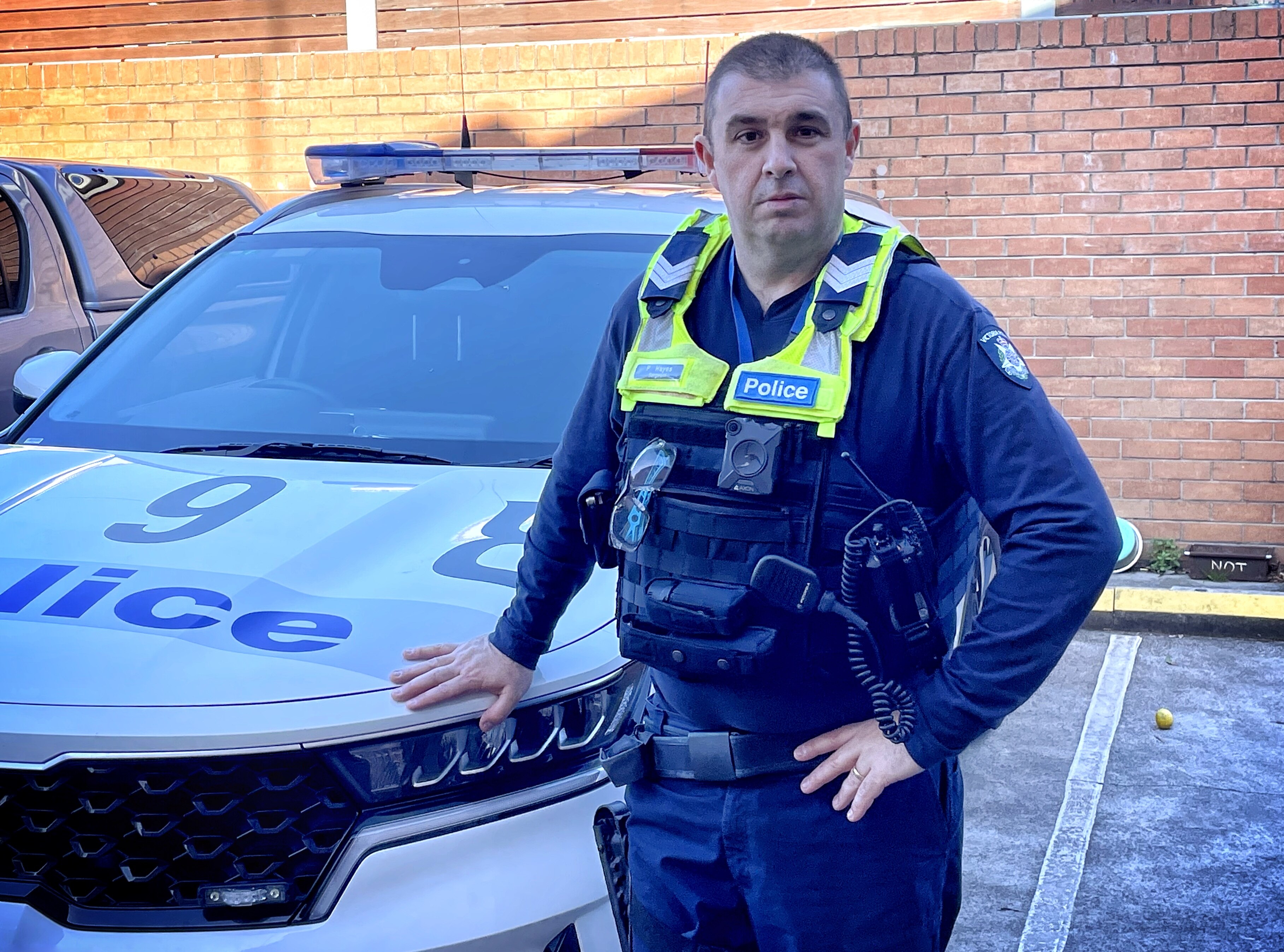 A police officer in uniform standing with one hand on the bonnet of his police car. 