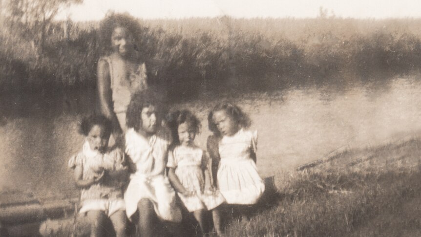 Five children pose for a group photo next to a waterway in a rural setting.