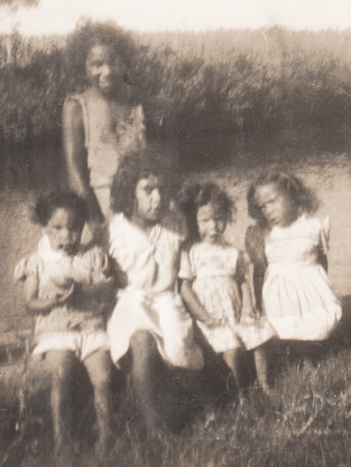 Five children pose for a group photo next to a waterway in a rural setting.