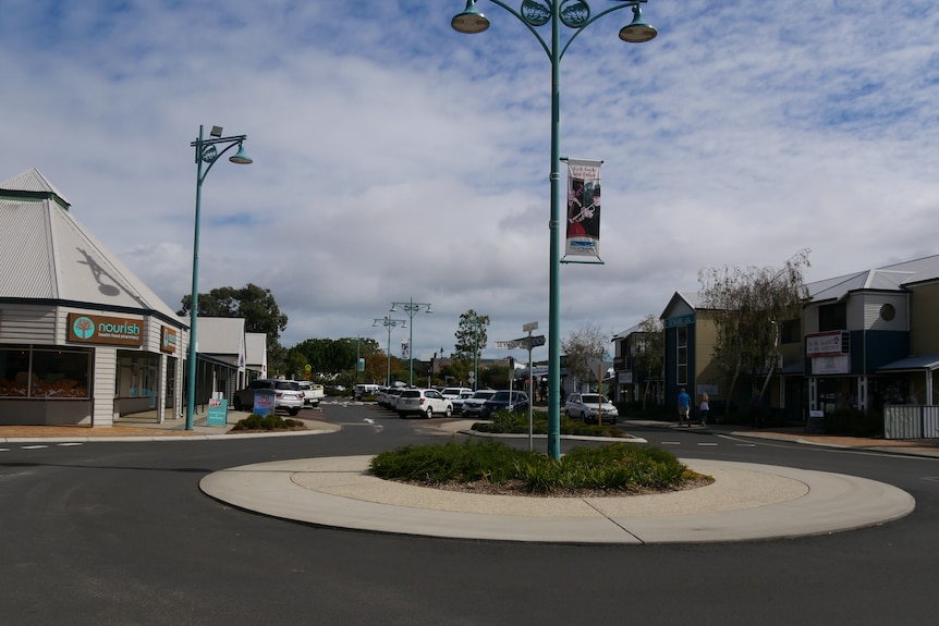 A roundabout on a street with one to two-storey shops along it. 