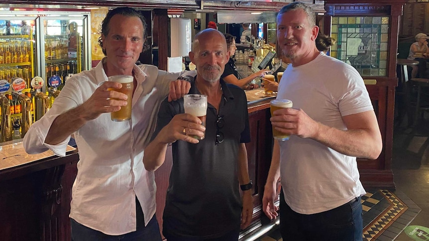 three men toasting a beer in a bar
