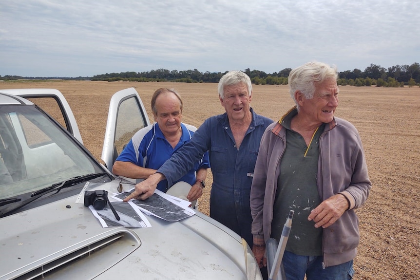Three men look at maps on the bonnet of a white ute. 