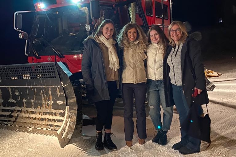 A group of four women smile as they pose next to a snow plough.