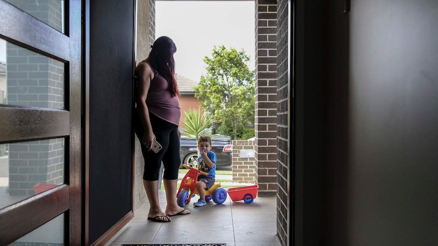 A woman looks down at a young boy, who is seated on a tricycle and looking at the camera