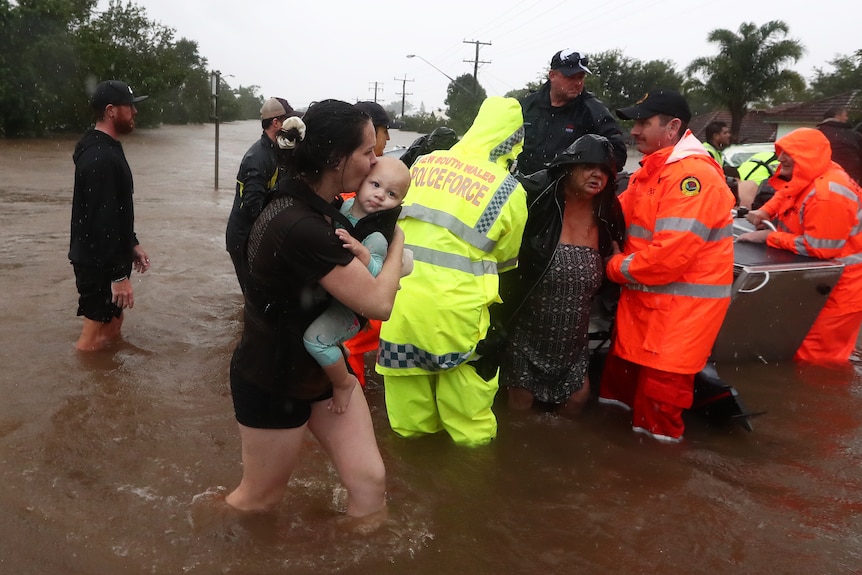 a woman holding a baby as another woman is lifted from a dhingy after a flood rescue