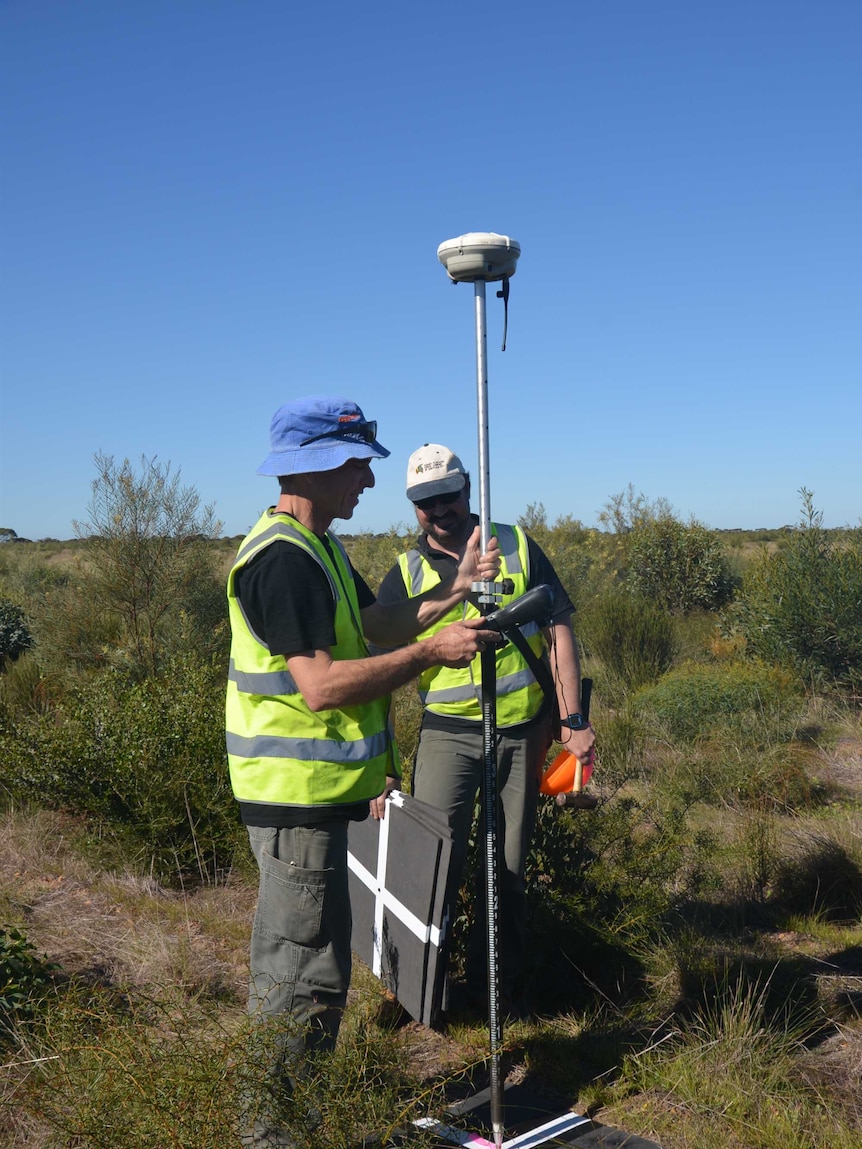 Two men standing in a paddock with aerial surveying equipment.