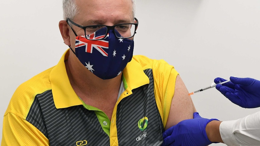 Scott Morrison, wearing an Australia flag face mask, is giving a vaccine jab in his arm by a nurse.