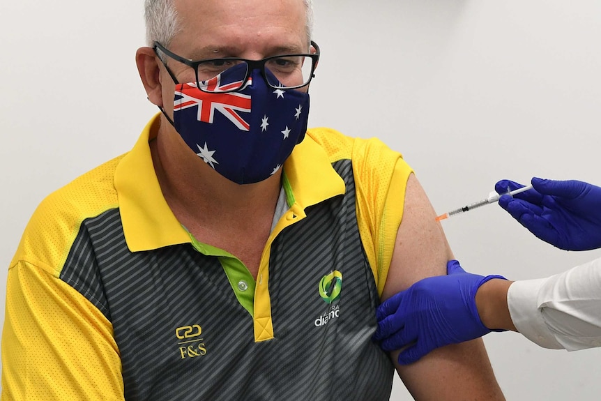 Scott Morrison, wearing an Australia flag face mask, is giving a vaccine jab in his arm by a nurse.